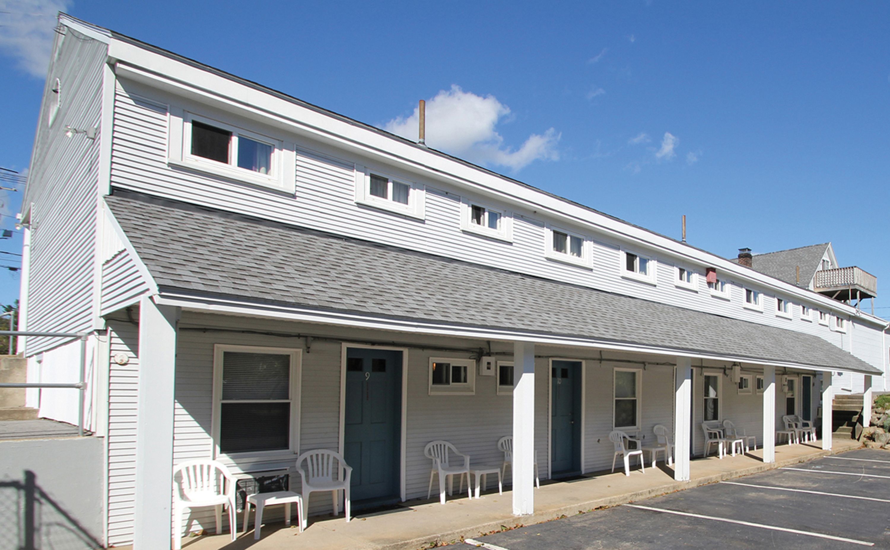 A two-story building with a flat roof, white siding, and a covered front porch with white plastic chairs.