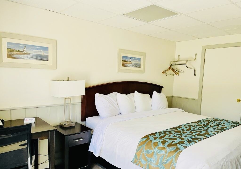 A hotel room with a bed, a desk, a chair, a lamp, and two framed pictures on the wall.