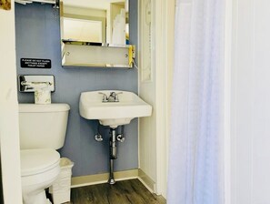 Un bagno con il water, un lavandino e un cartello che indica di non gettare nello scarico altro che carta igienica.