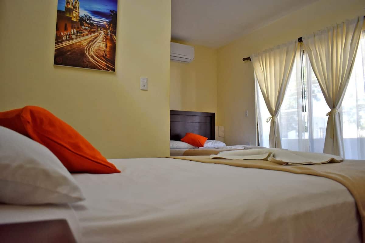 A hotel room with two beds, a painting on the wall, an air conditioning unit, and curtains on the window.
