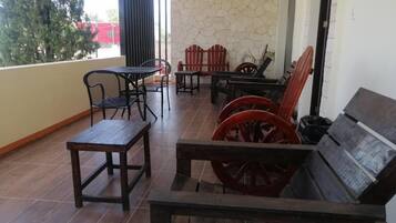 Un patio cubierto con mesas y sillas de madera, un muro de piedra y vistas a un edificio rojo.