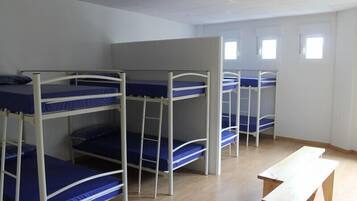 A dormitory room with bunk beds, a wooden bench, and a window.