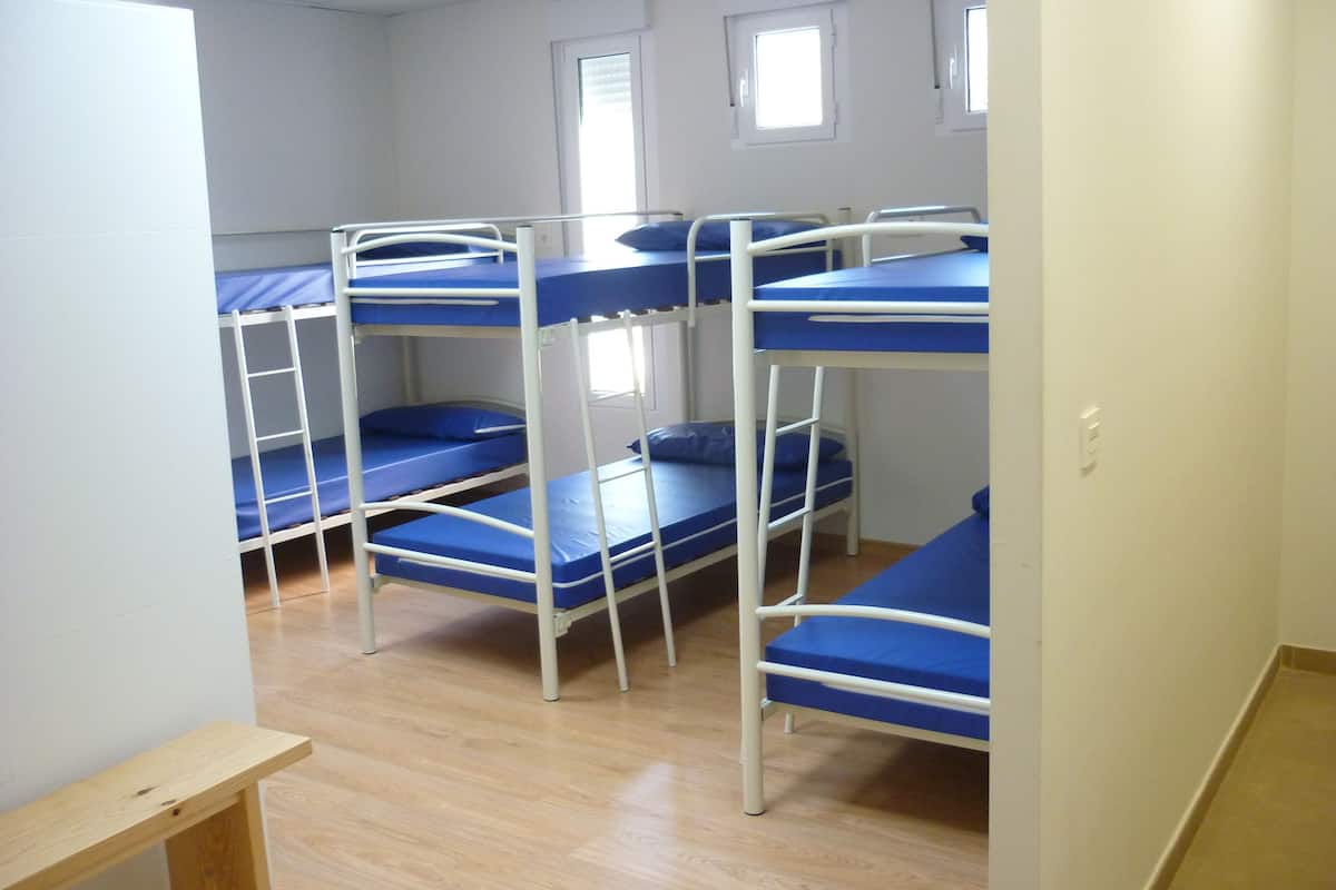 A dormitory room with bunk beds, wooden flooring, and white walls.