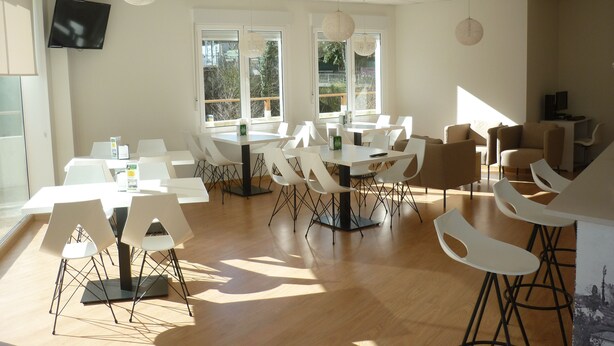 A spacious room with multiple tables and chairs, large windows with views of greenery, and hanging spherical light fixtures. - Pensión Albergue Puente Ribeira - Hostel (Sarria)