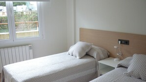A bedroom with two beds, each with a white bedspread and pillows, a bedside table with a lamp, and a window with a view of greenery outside. - Pensión Albergue Puente Ribeira - Hostel (Sarria)