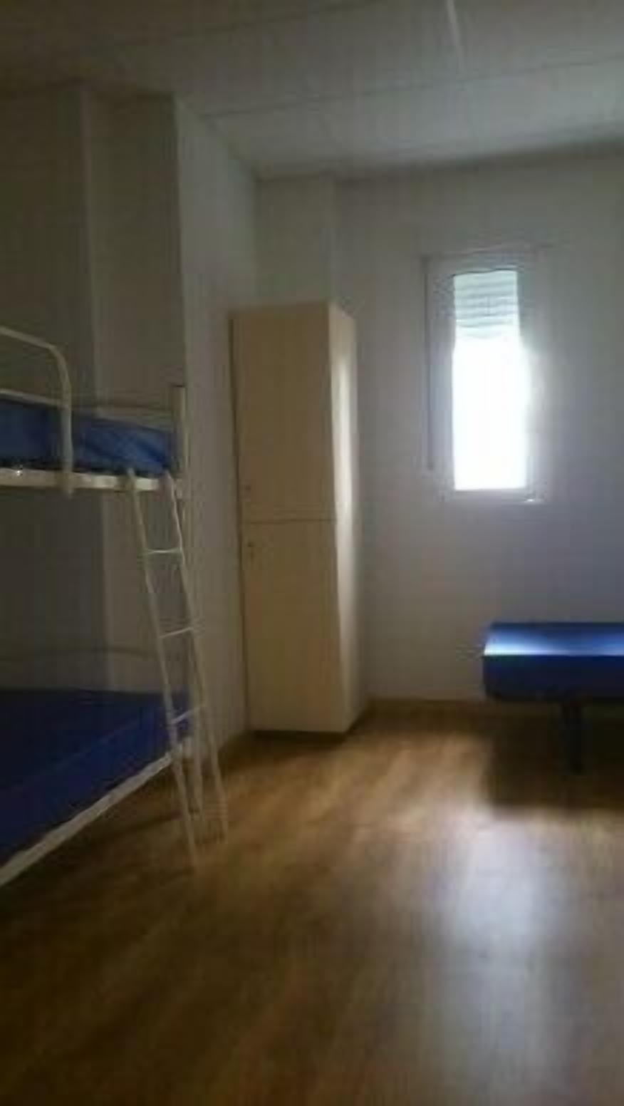 Een kamer met een stapelbed, een kledingkast en een klein raam.