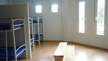 Una habitación con literas, un banco de madera y ventanas.