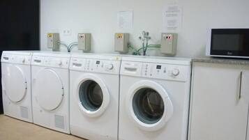 A row of four front-loading washing machines in a laundry room with a microwave on the counter.