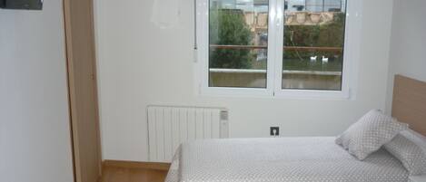 Un dormitorio con dos camas, una ventana que da a un edificio y follaje, un radiador y una puerta.