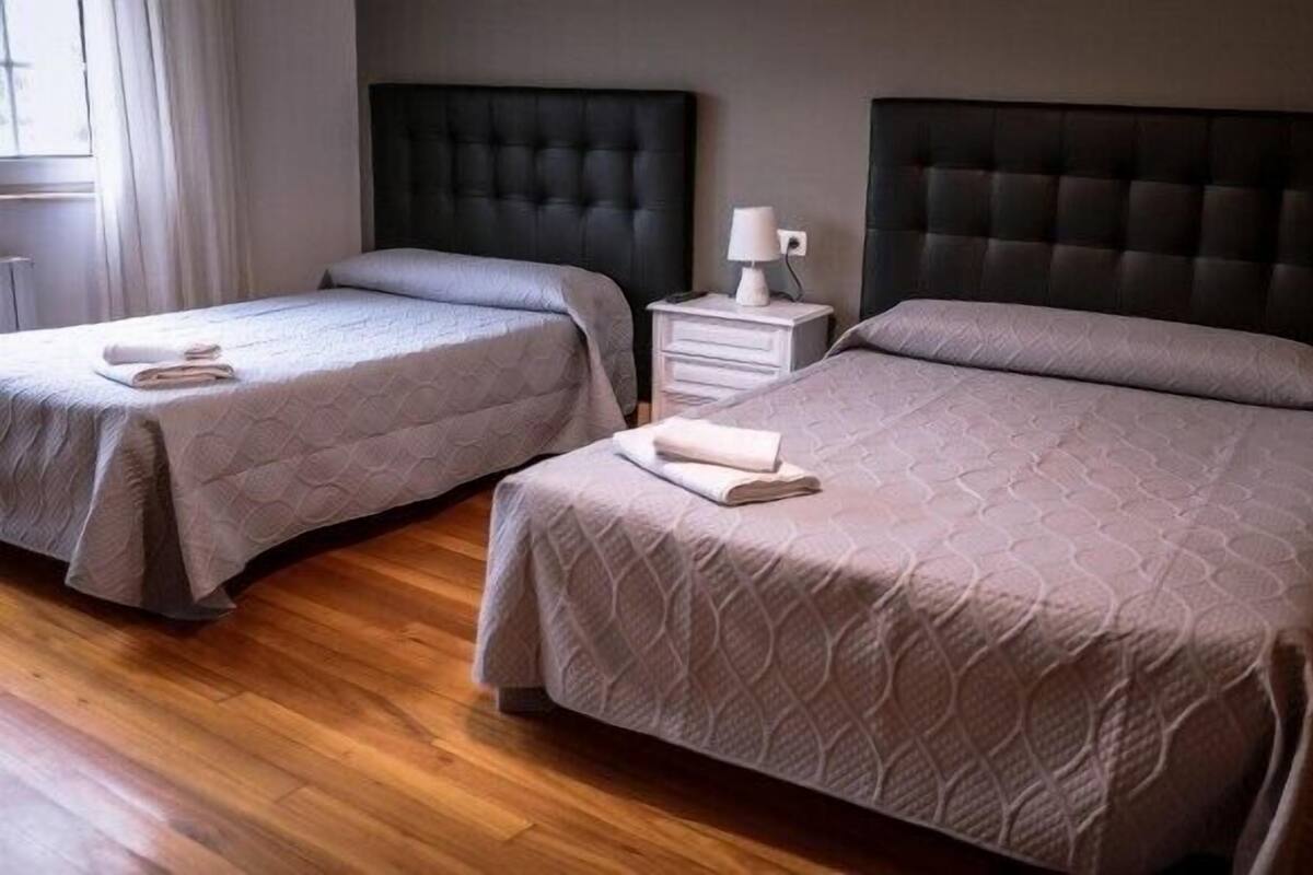 A hotel room with two beds, a nightstand with a lamp, and a window with curtains.