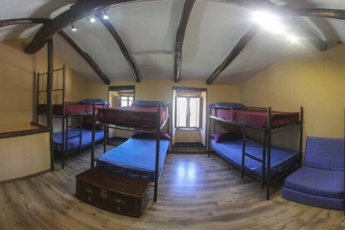 A dormitory room with four bunk beds, wooden flooring, and a small wooden chest.