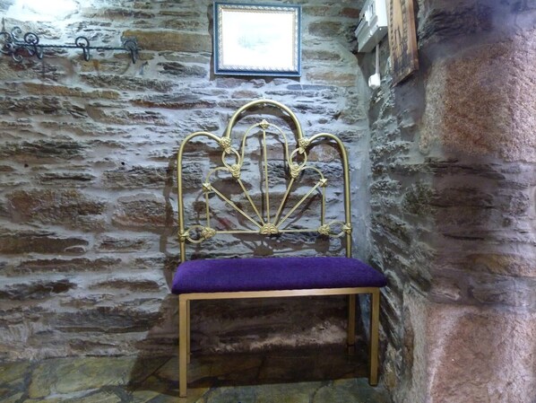 A stone wall with a metal bed frame and a purple cushion. - Pensión Albergue A Pedra (Sarria)