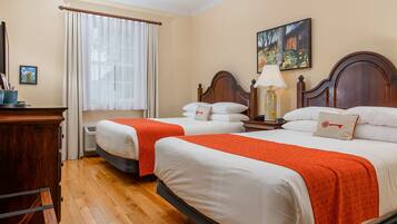 A hotel room with two beds, a wooden dresser, a window with curtains, and a painting on the wall.