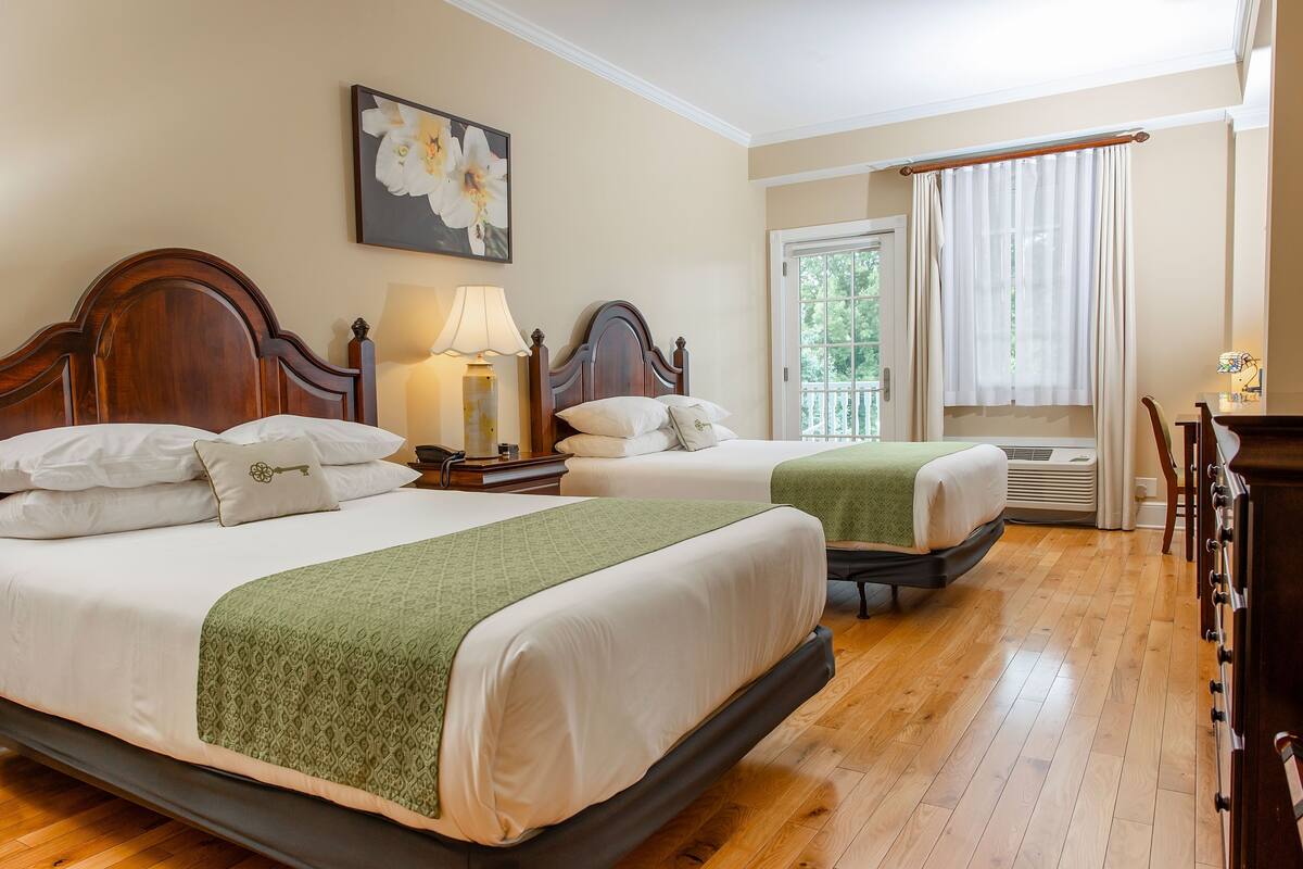 Una habitación de hotel con dos camas, un cuadro, una ventana con cortinas y suelo de madera.