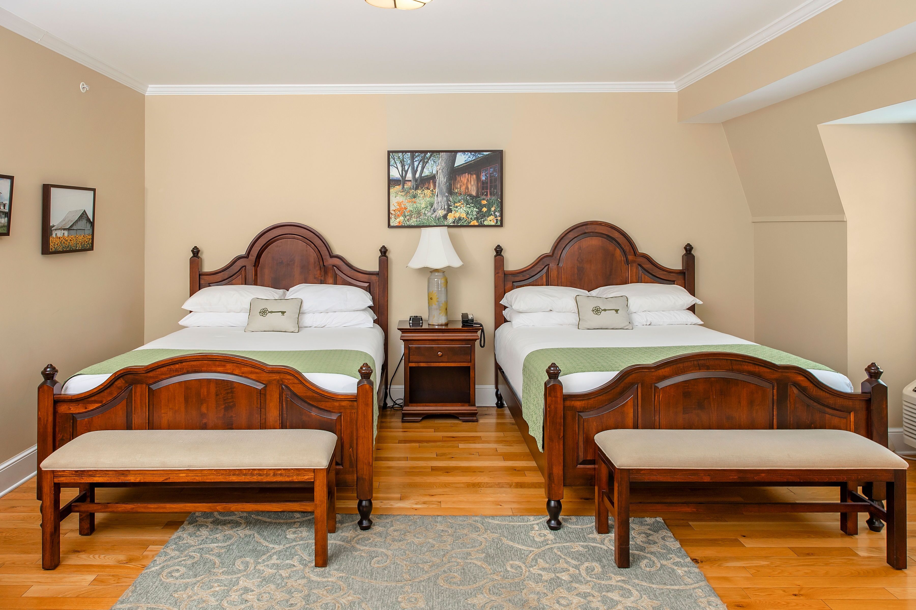 A double room with two wooden beds, a nightstand, a bench, and a painting on the wall.