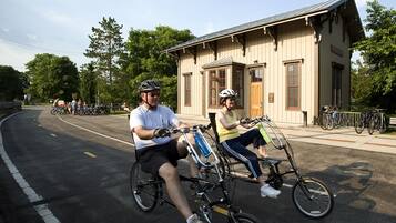 Two people on bicycles in front of a building with a beige facade and a red door.
