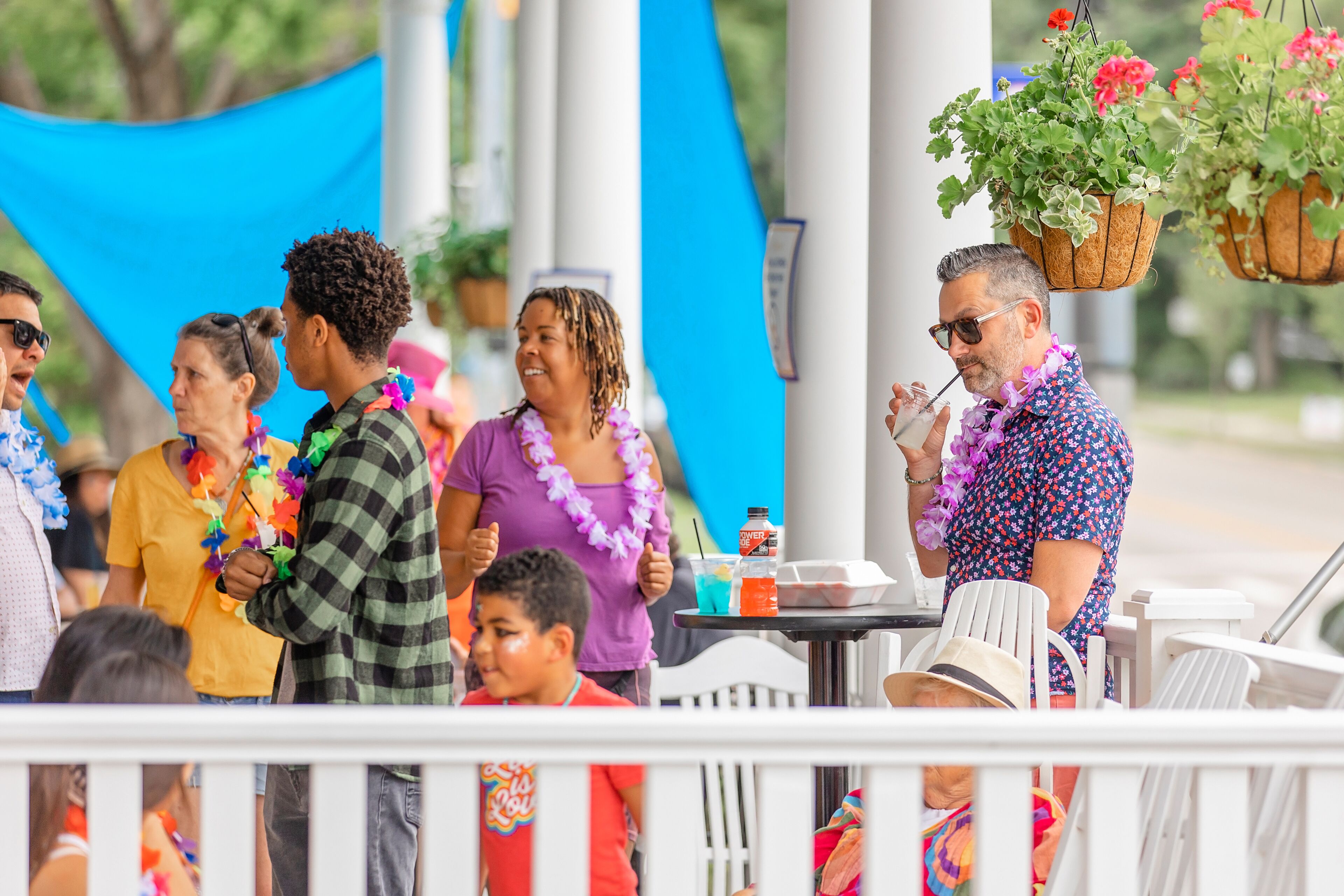 A group of people at an outdoor event with tables and chairs, some wearing leis.