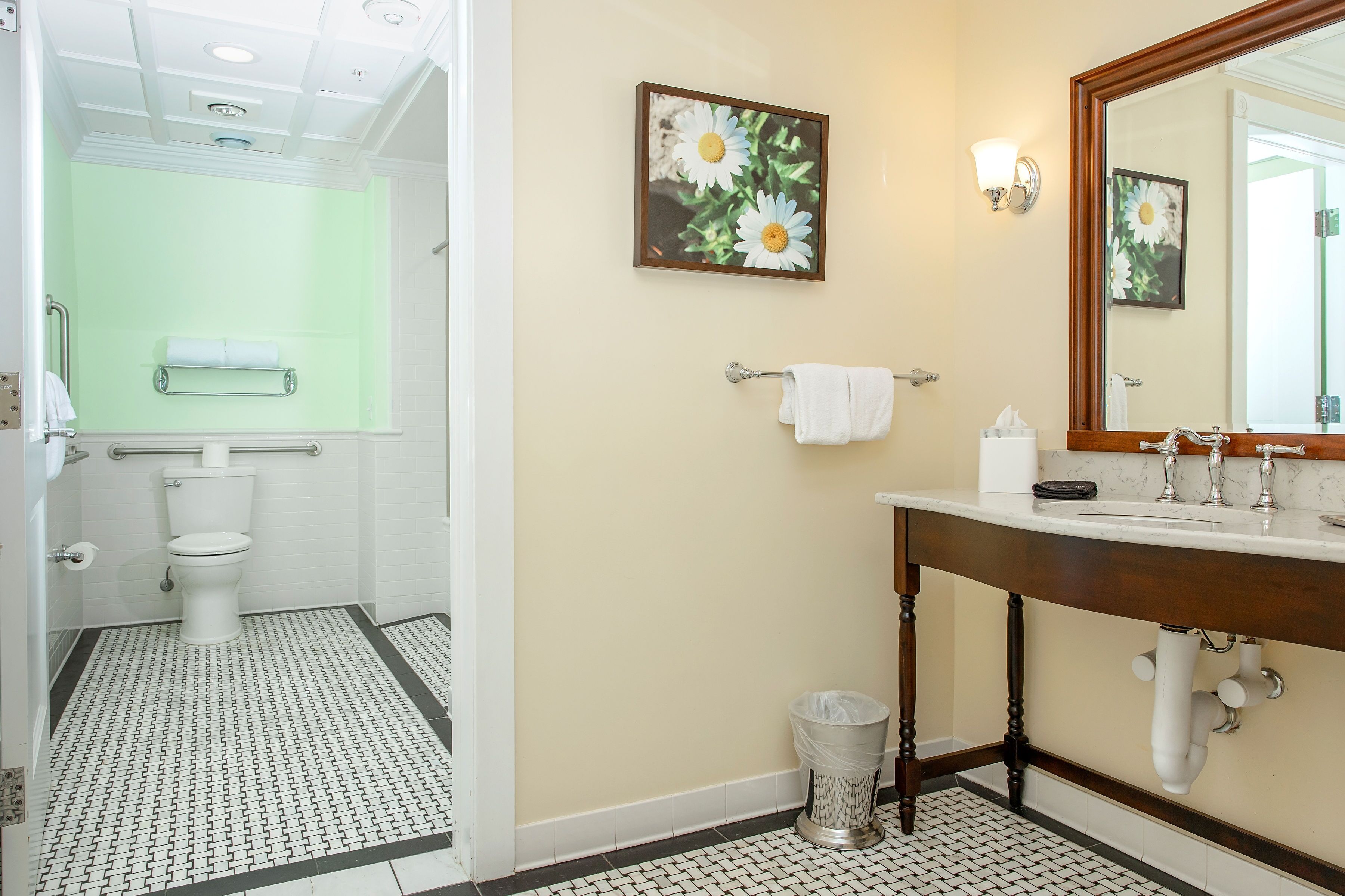 Une salle de bain avec des toilettes, un lavabo et un miroir. Deux serviettes sont suspendues à des porte-serviettes.