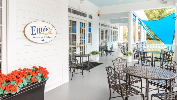 A covered outdoor area with tables and chairs, a sign for Ellie's Restaurant & Bakery, and a blue sky visible through the windows.