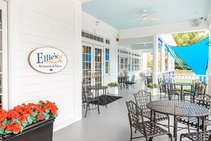 Un’area esterna coperta con tavoli e sedie, un cartello per Ellie's Restaurant & Bakery e un cielo azzurro visibile attraverso le finestre.