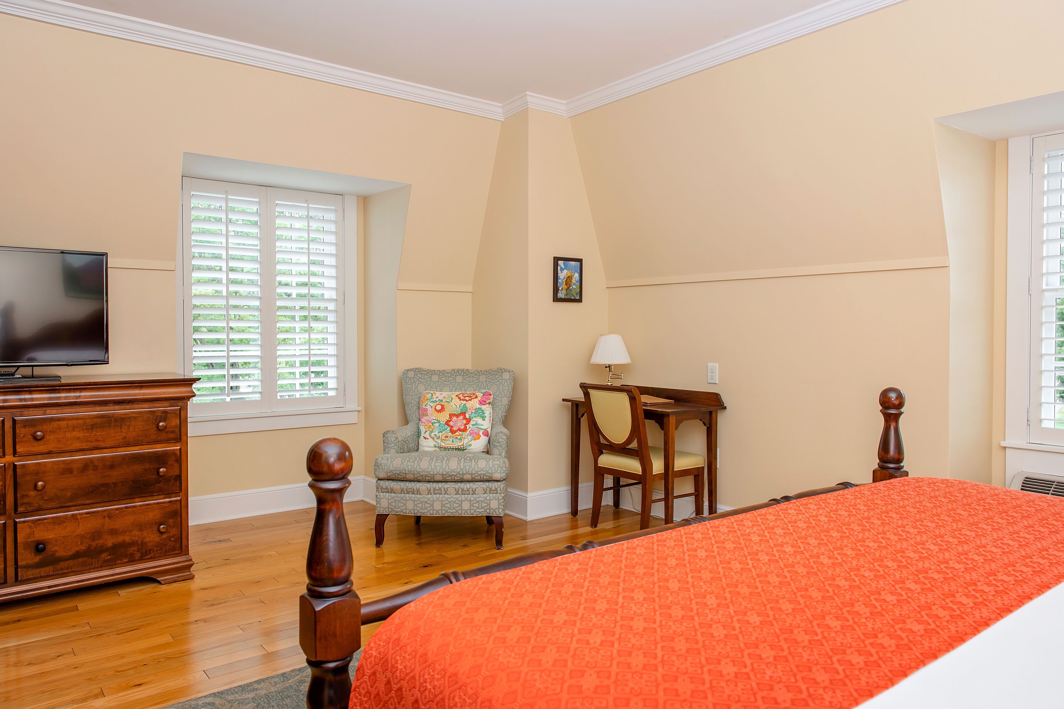 A bedroom with a bed, dresser, TV, chair, and desk.