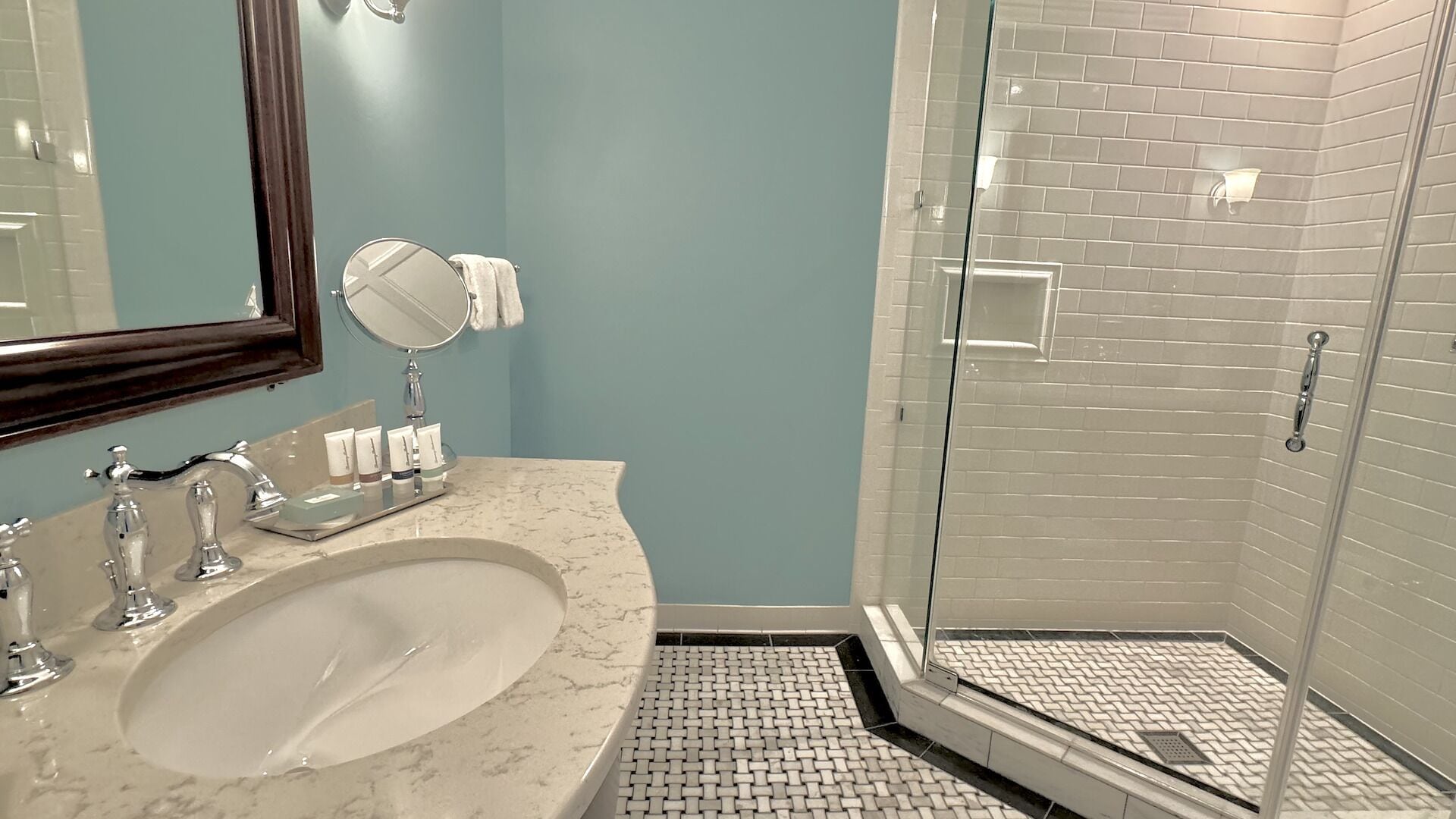 A bathroom with a marble sink, a round mirror, and a glass shower enclosure.
