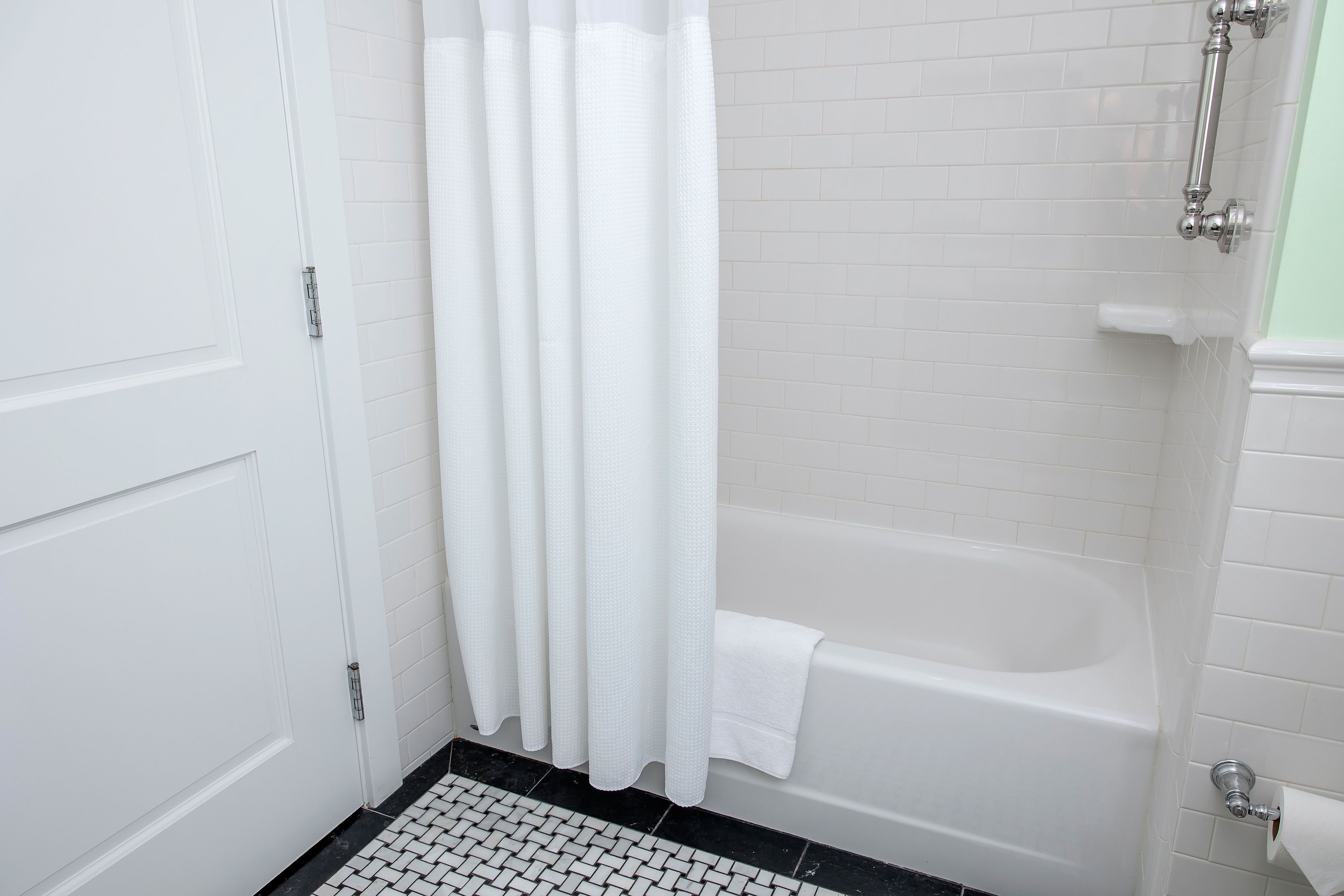 Un baño con una bañera blanca, una puerta blanca y un suelo de baldosas blanco y negro.