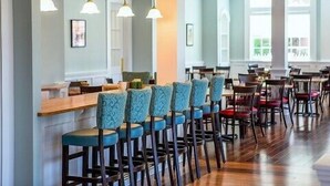 A spacious restaurant with high ceilings, wooden floors, and a long counter with bar stools.