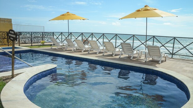 Une piscine à l’eau d’un bleu cristallin, entourée de chaises longues et de parasols jaunes, avec vue sur l’océan.