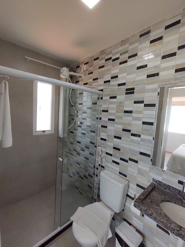A modern bathroom with a glass-enclosed shower, a white toilet, and a granite countertop with a sink.