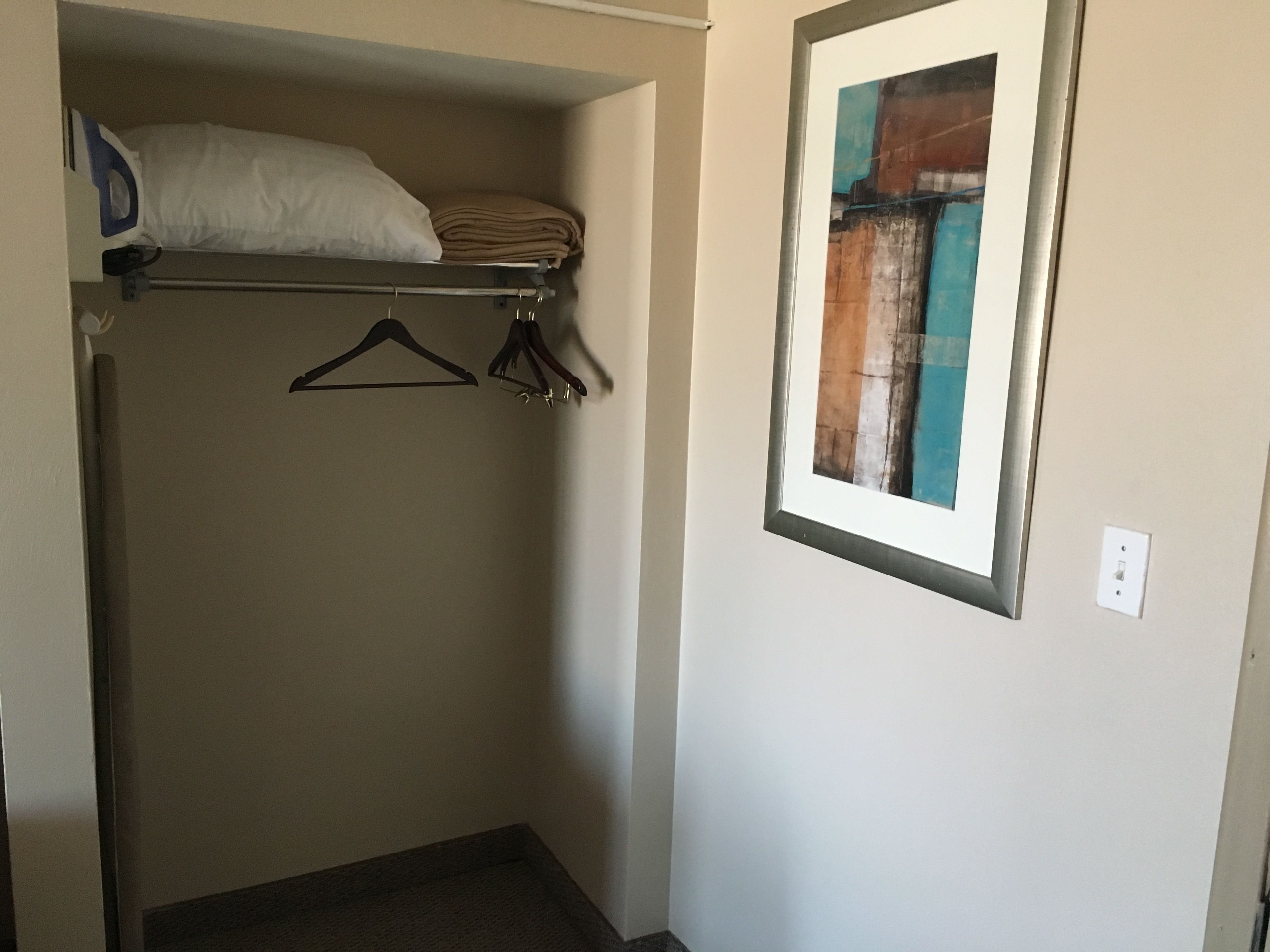 A small, enclosed closet with a hanging rod, a folded towel, and a pillow on a shelf.