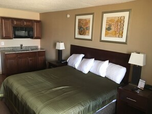 A hotel room with a bed, a nightstand, a lamp, a desk with a lamp, a microwave, and a sink. - Allen Park Motor Lodge (Allen Park)