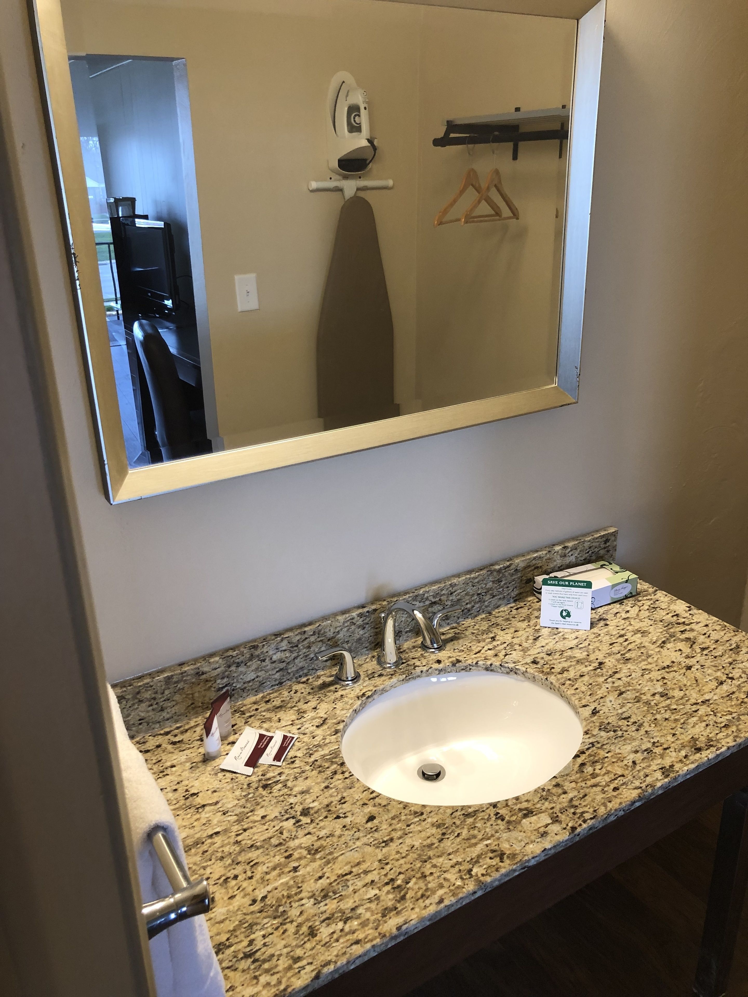 Un baño con encimera de granito, un lavabo blanco y un espejo grande.