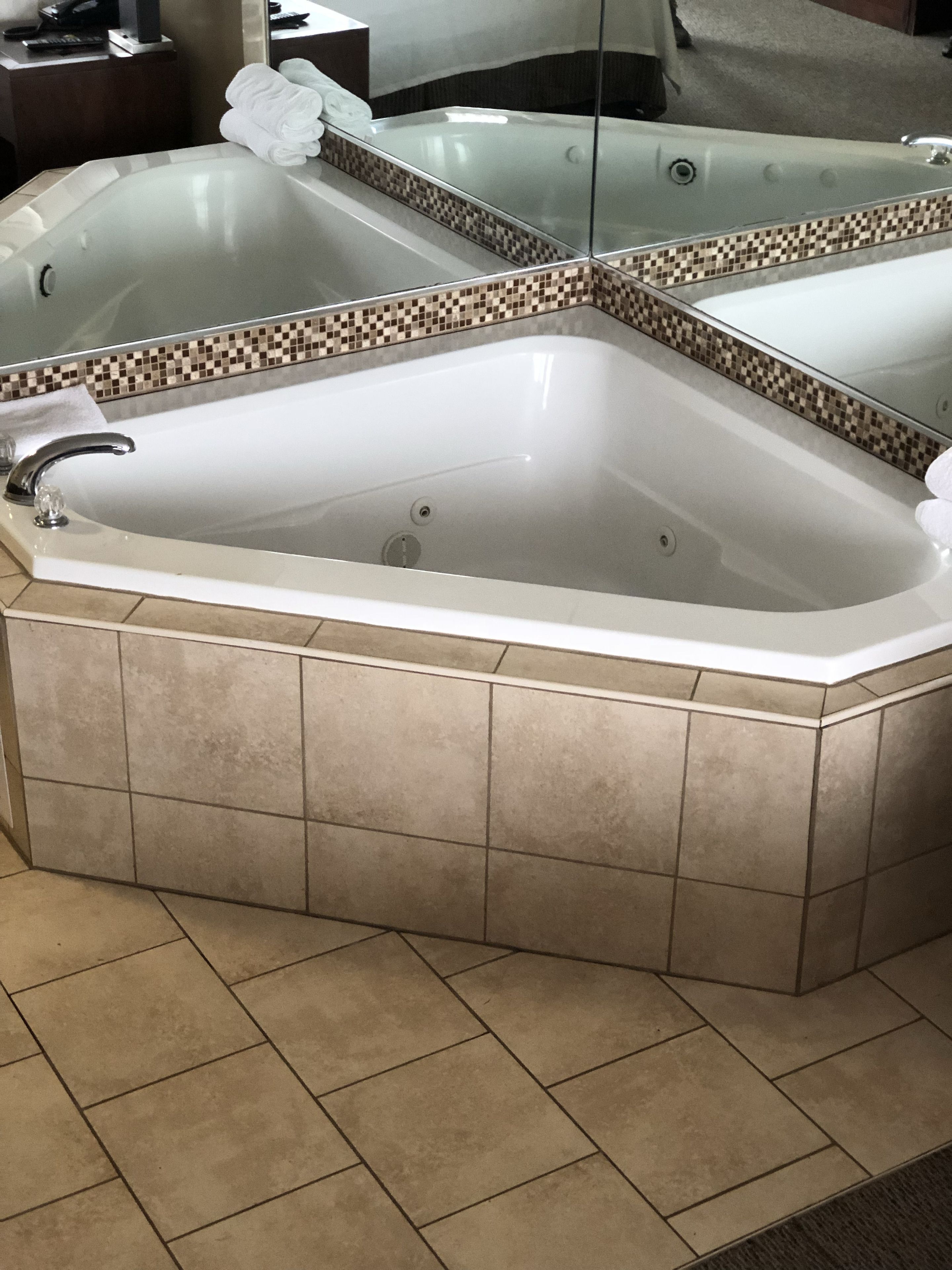 Una bañera en esquina con un revestimiento de azulejos y un espejo encima.