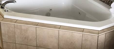 Una bañera en esquina con un revestimiento de azulejos y un espejo encima.