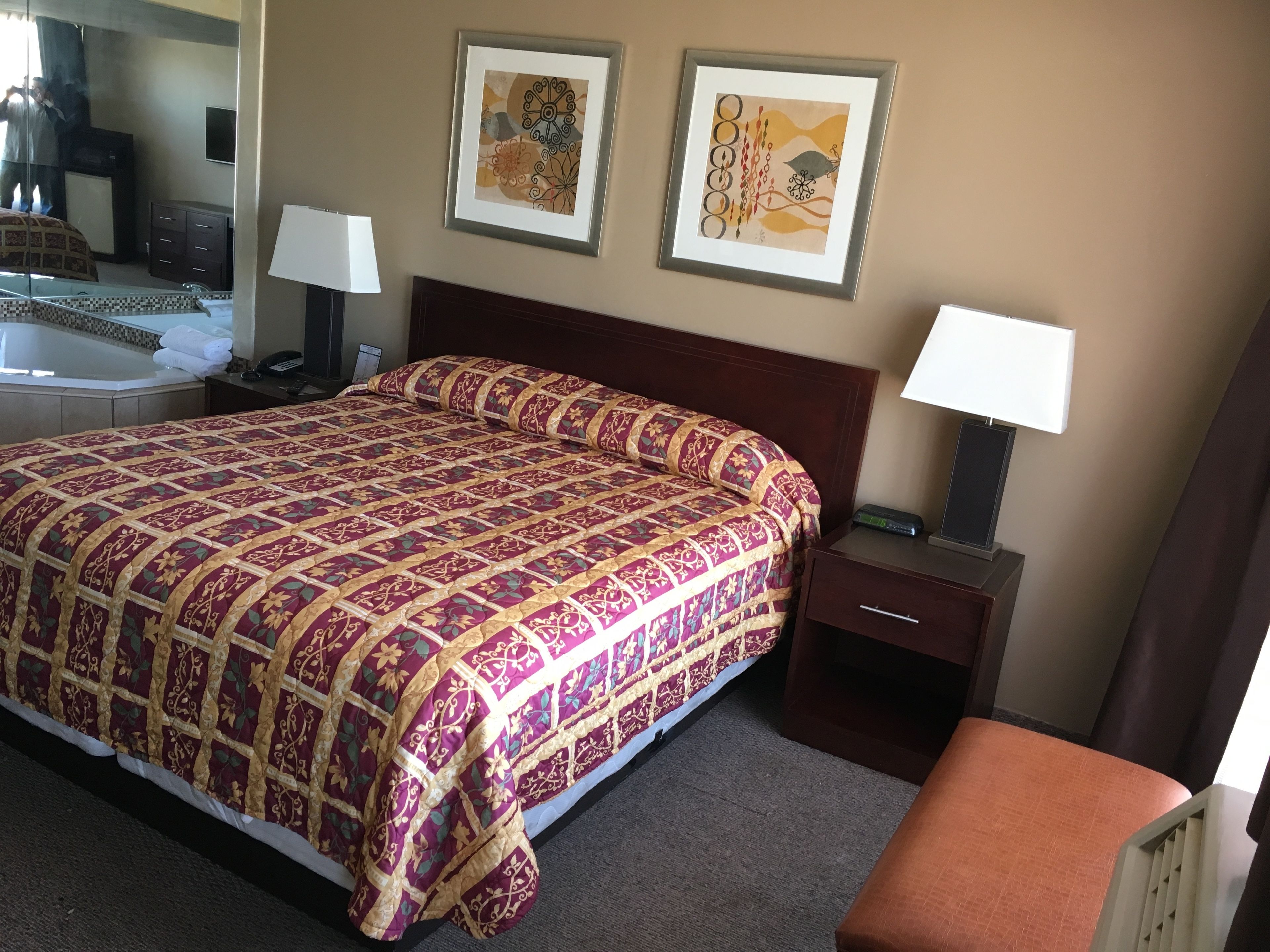 A hotel room with a large bed, two bedside tables, a nightstand, a mirror, and two framed artworks on the wall.