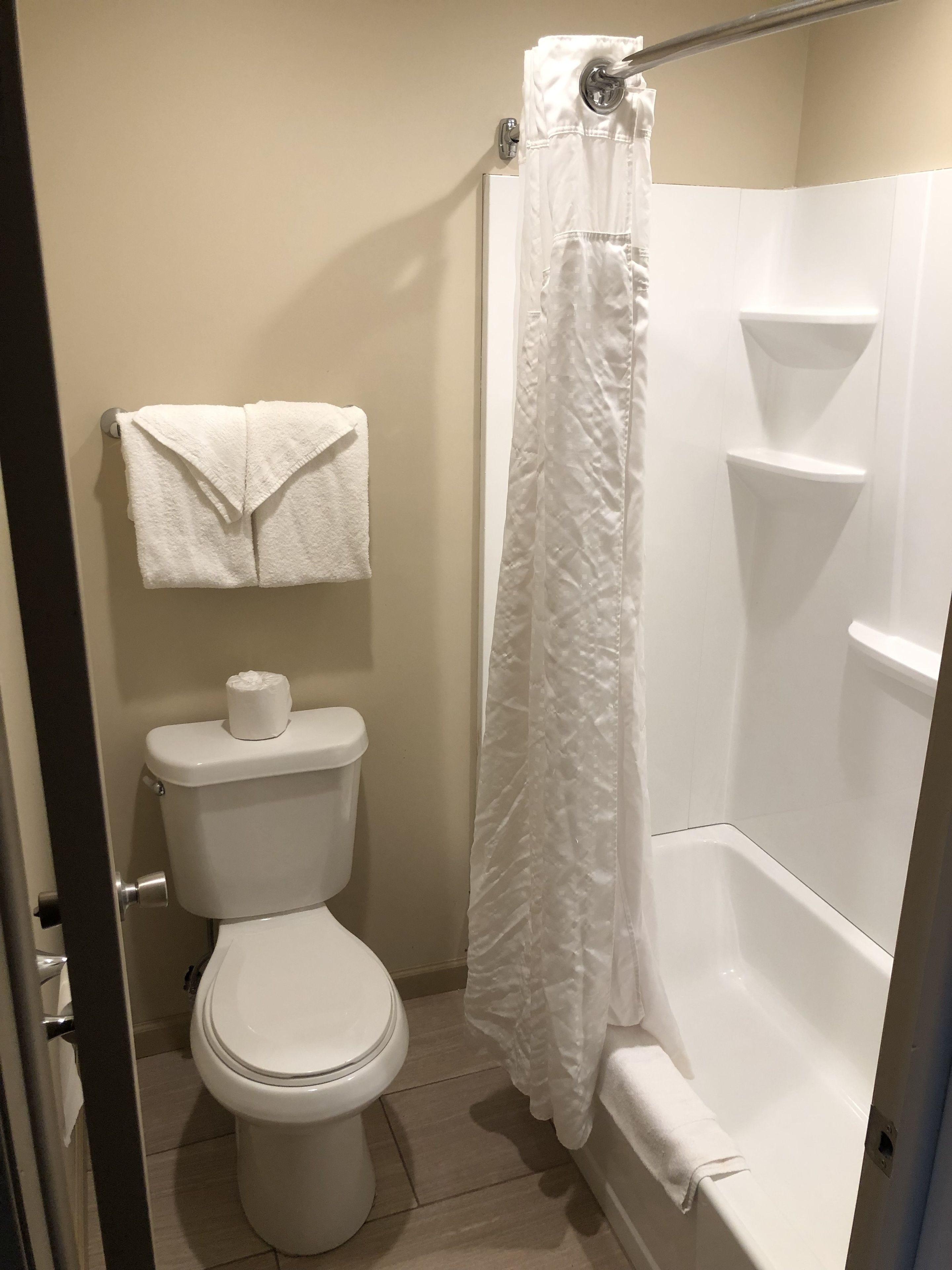 A bathroom with a toilet, a towel rack with a folded towel, a shower curtain, and a bathtub.