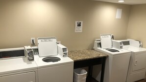 A laundry room with two front-loading washers and dryers, a granite countertop, and a trash can.