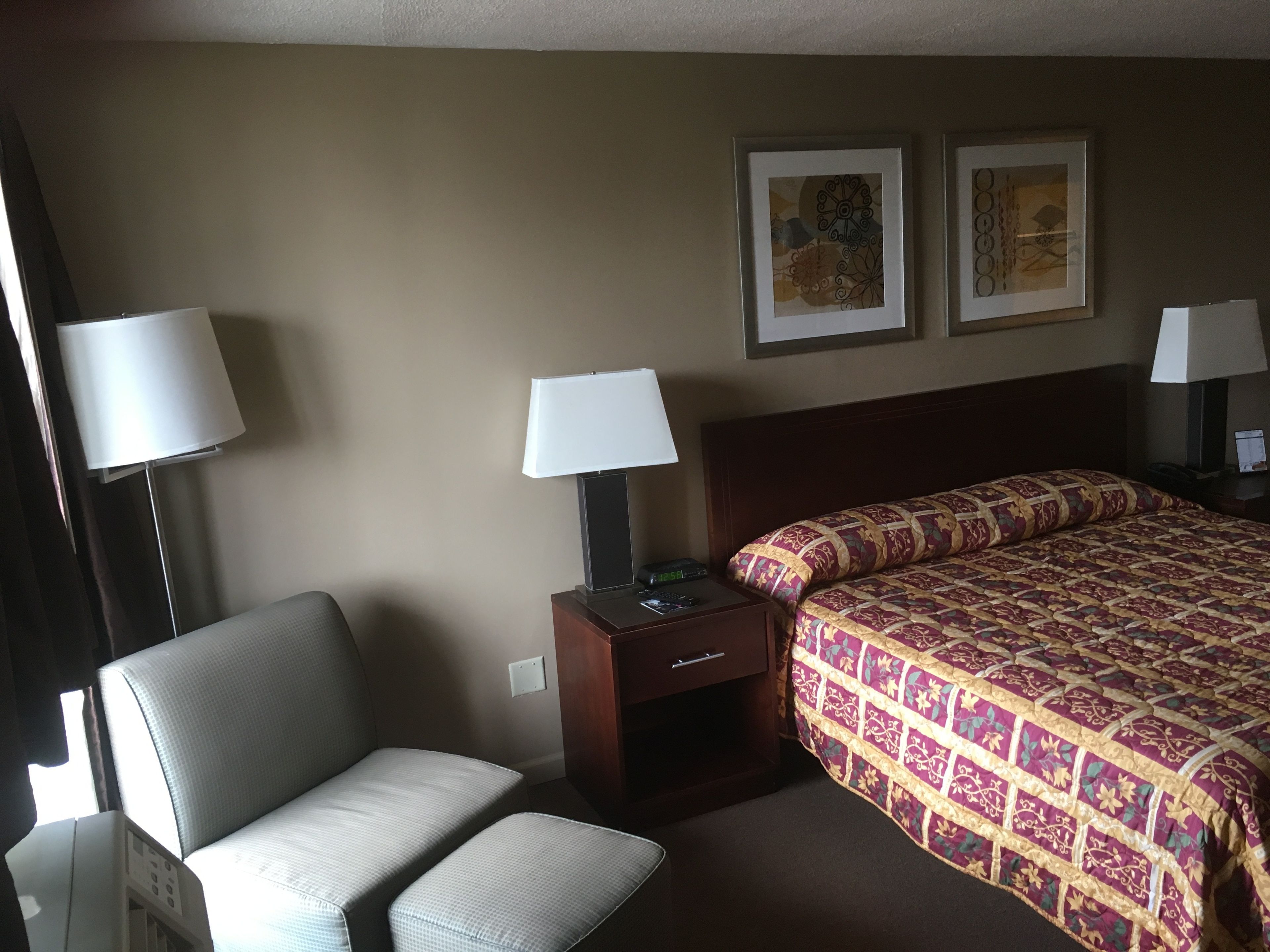 A hotel room with a bed, a chair, a nightstand, and two wall-mounted lamps.