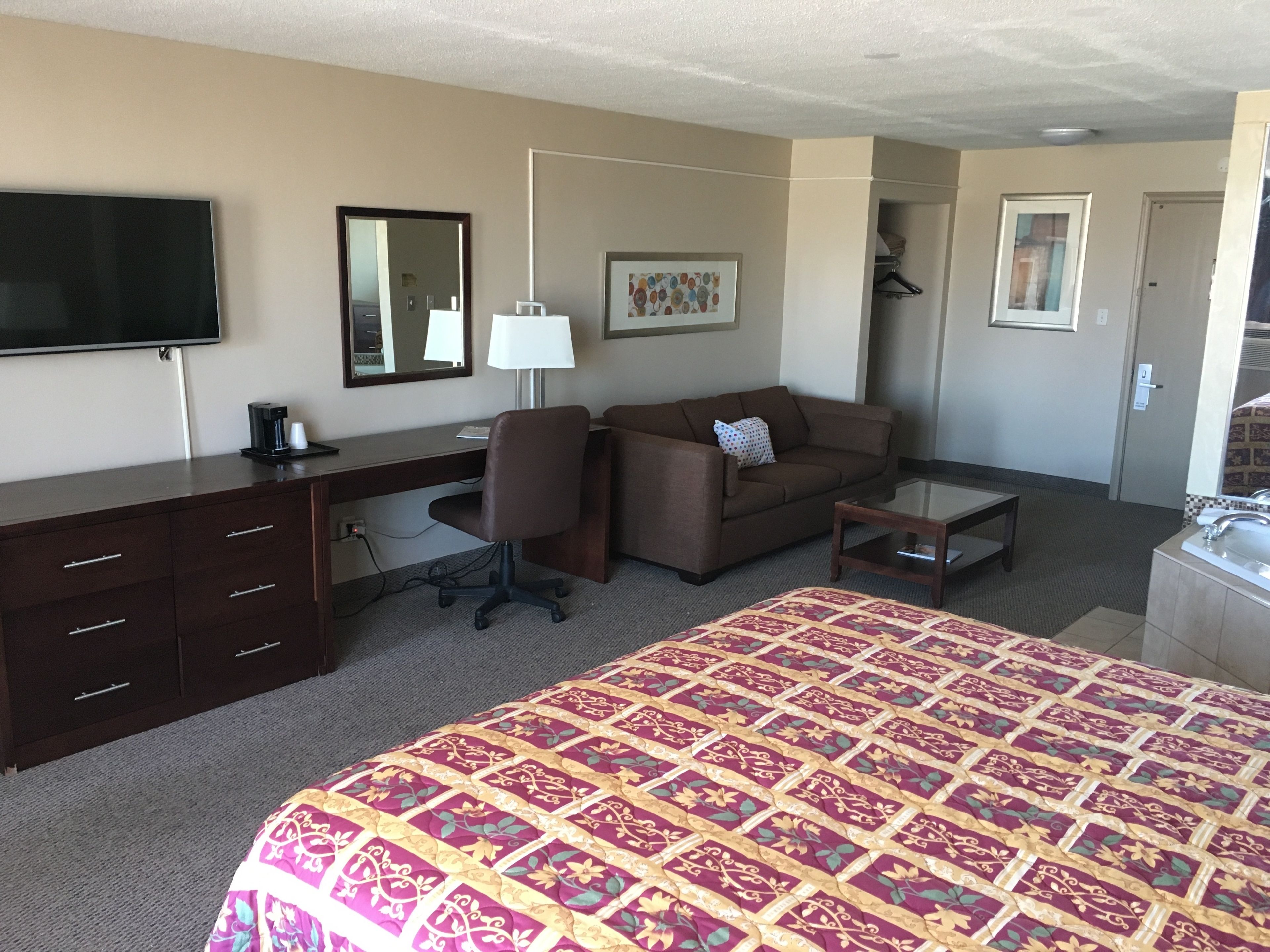 Camera d'albergo con un letto, una scrivania, una sedia, un divano, una TV, una lampada e un bagno.