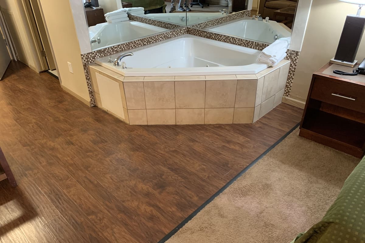 A bathroom with a large freestanding bathtub, a mirror, and a wooden floor.