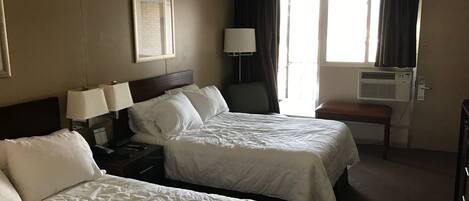 Habitación de hotel con dos camas, un escritorio, una silla, una ventana con cortinas y un equipo de aire acondicionado.