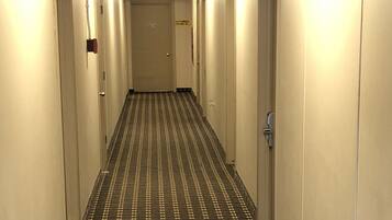 Un corridoio d'hotel con tappeto a motivi e porte su entrambi i lati, con un segnale di USCITA sopra le porte.