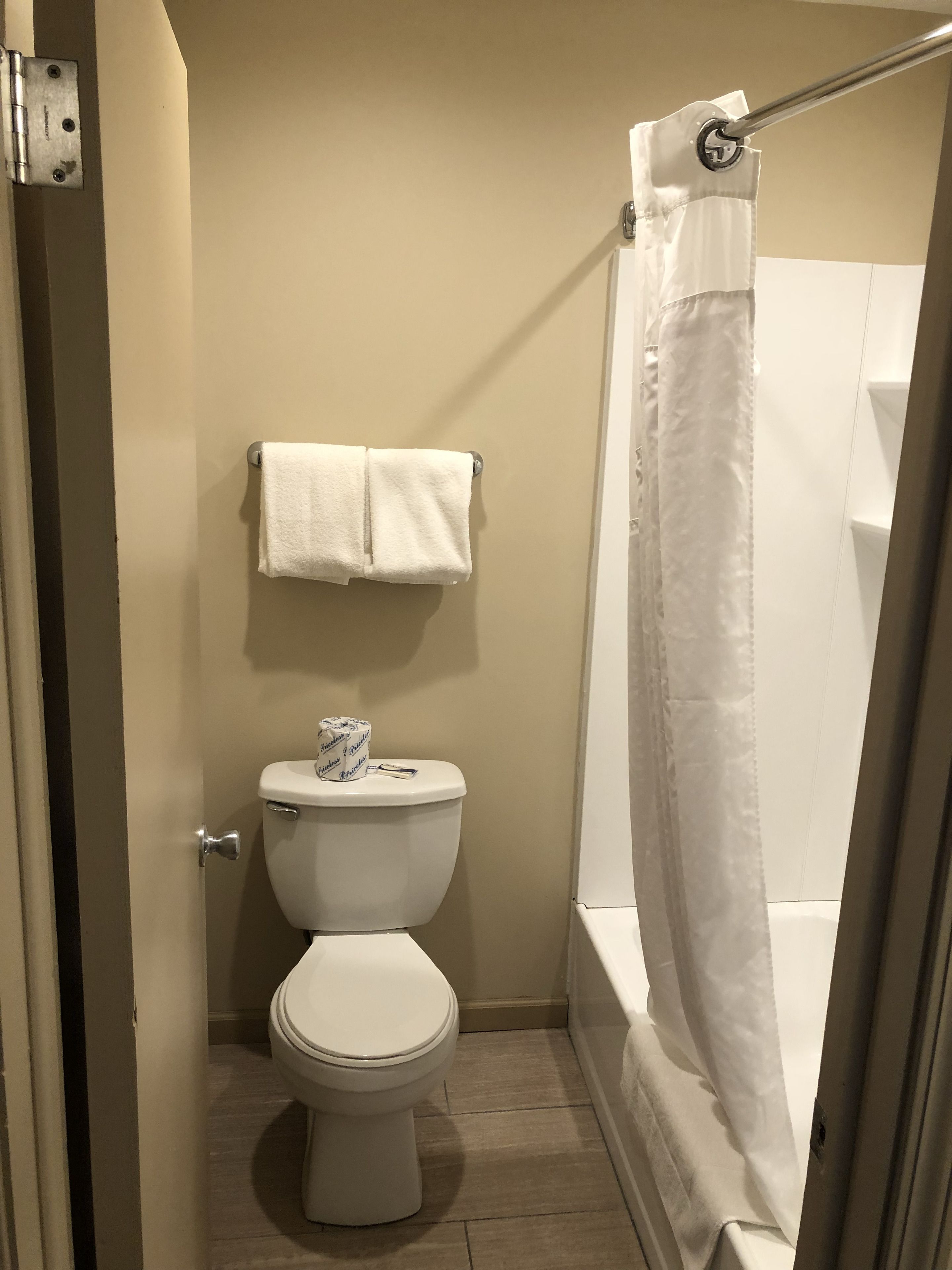 Un baño con inodoro, toallero con dos toallas, cortina de ducha y rollo de papel higiénico.