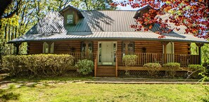 A log cabin with a porch, surrounded by greenery and trees.