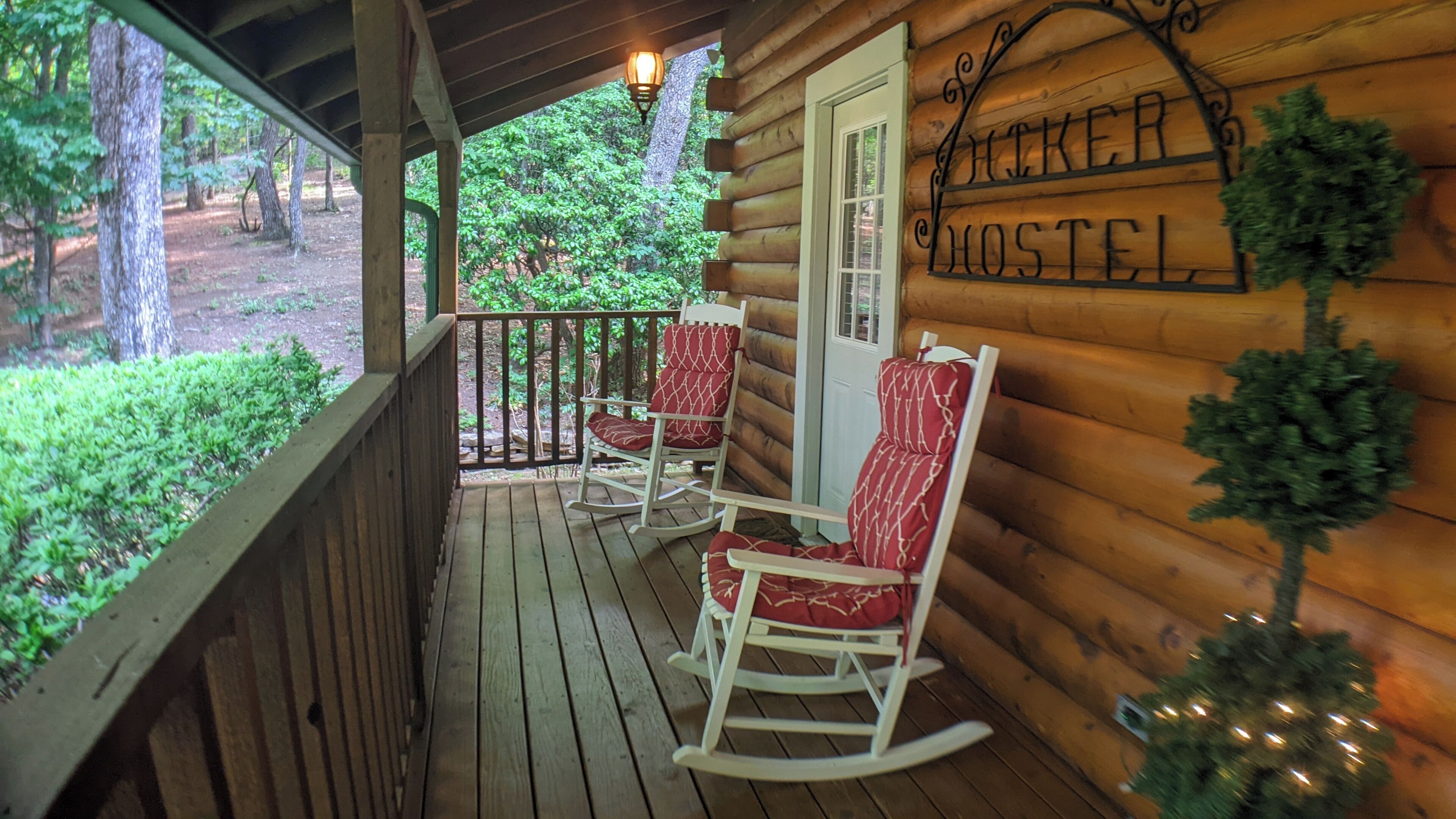 A wooden log cabin with a porch featuring rocking chairs and a sign reading "Jocker Motel".