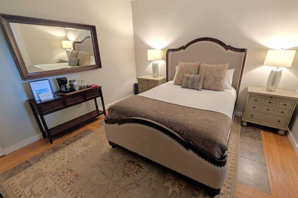 Um quarto com cama, mesas de cabeceira, cômoda, espelho e tapete.