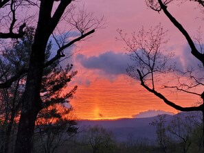 A sunset over a mountainous landscape with trees silhouetted against the sky.