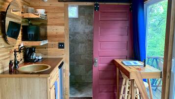 Interior em madeira com cozinha, uma porta vermelha e vista para o verde lá fora.