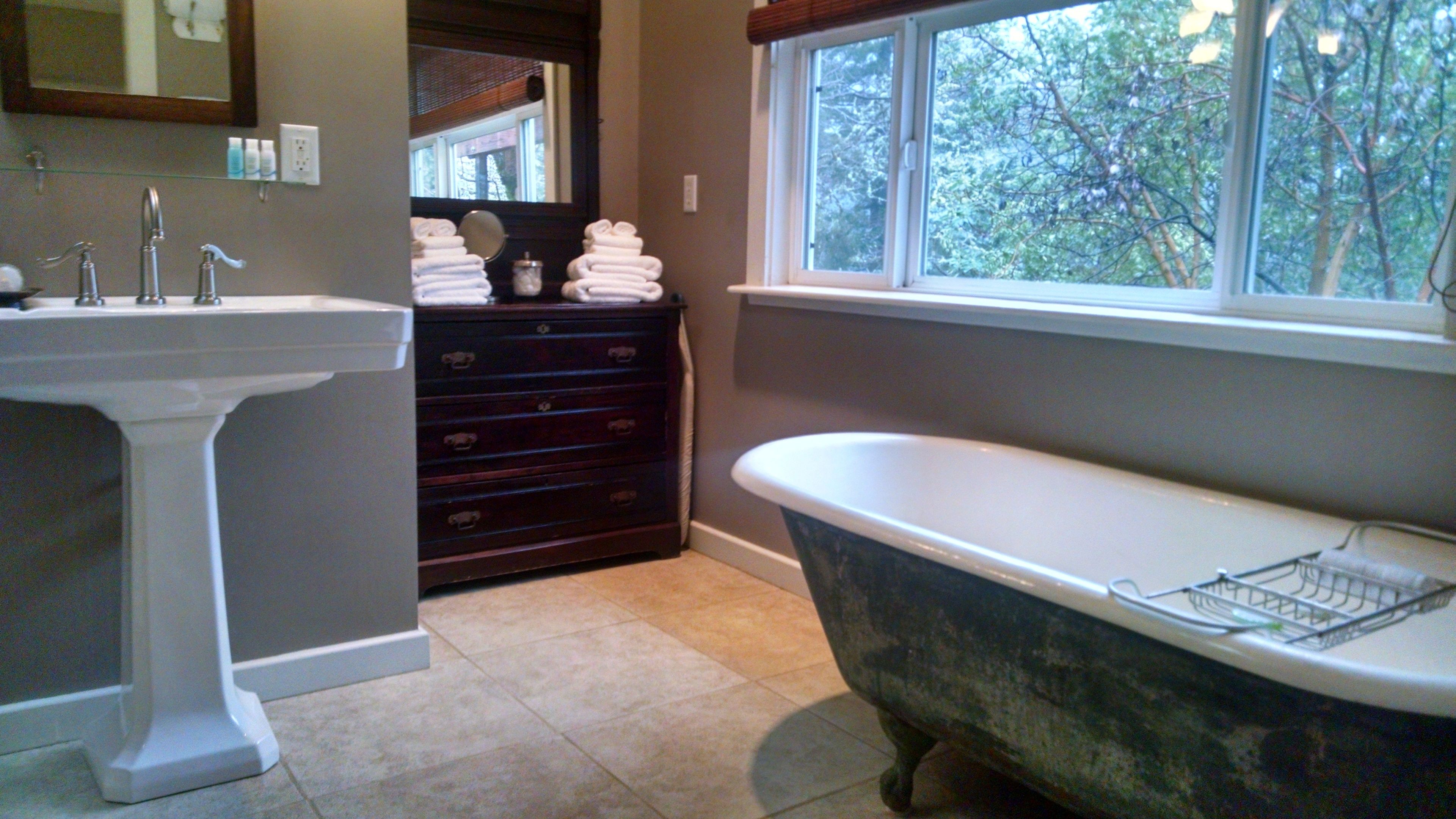A bathroom with a freestanding bathtub, a pedestal sink, and a dark wooden dresser.